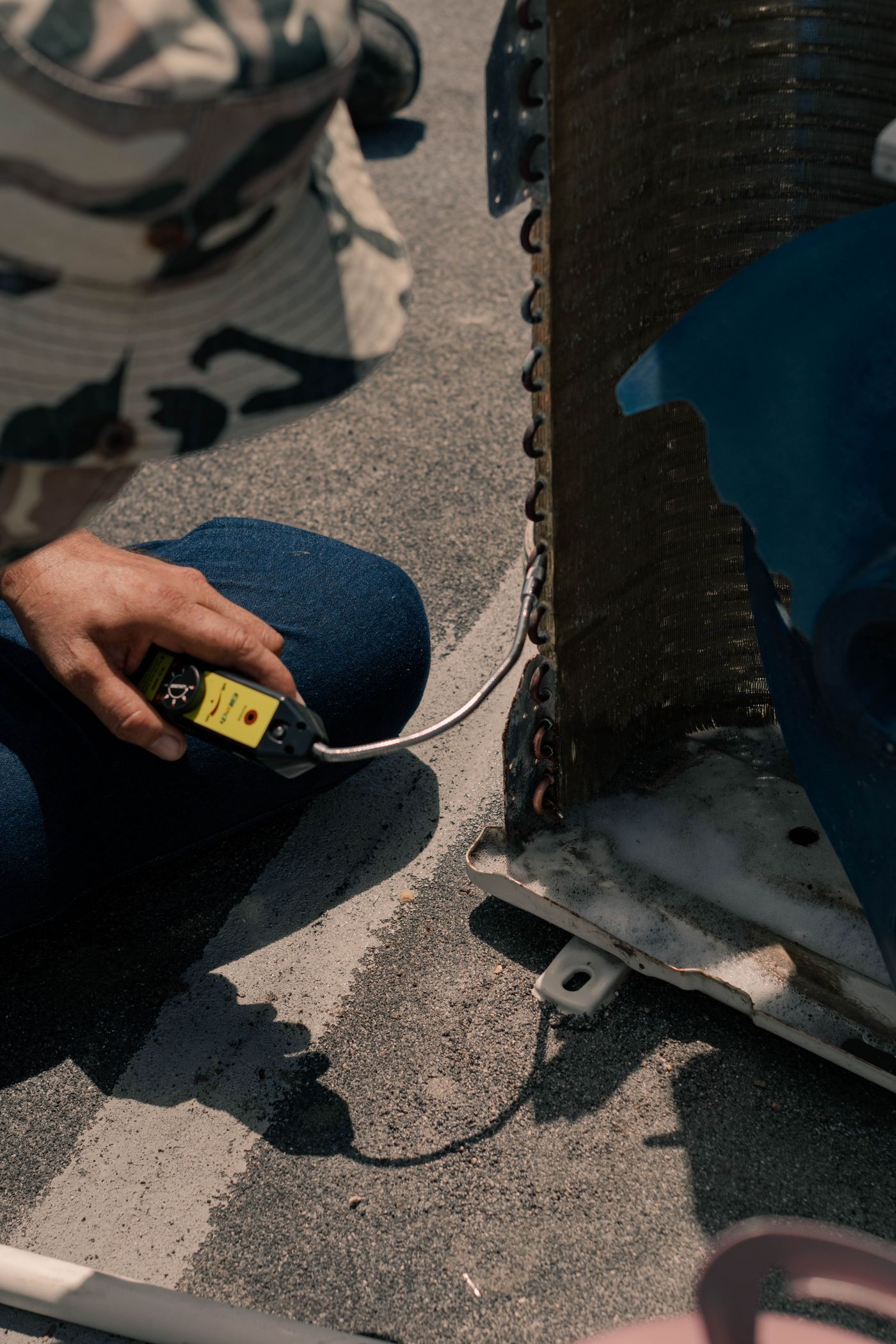 A technician holding a handheld leak detector against the coil of an outdoor air conditioning unit